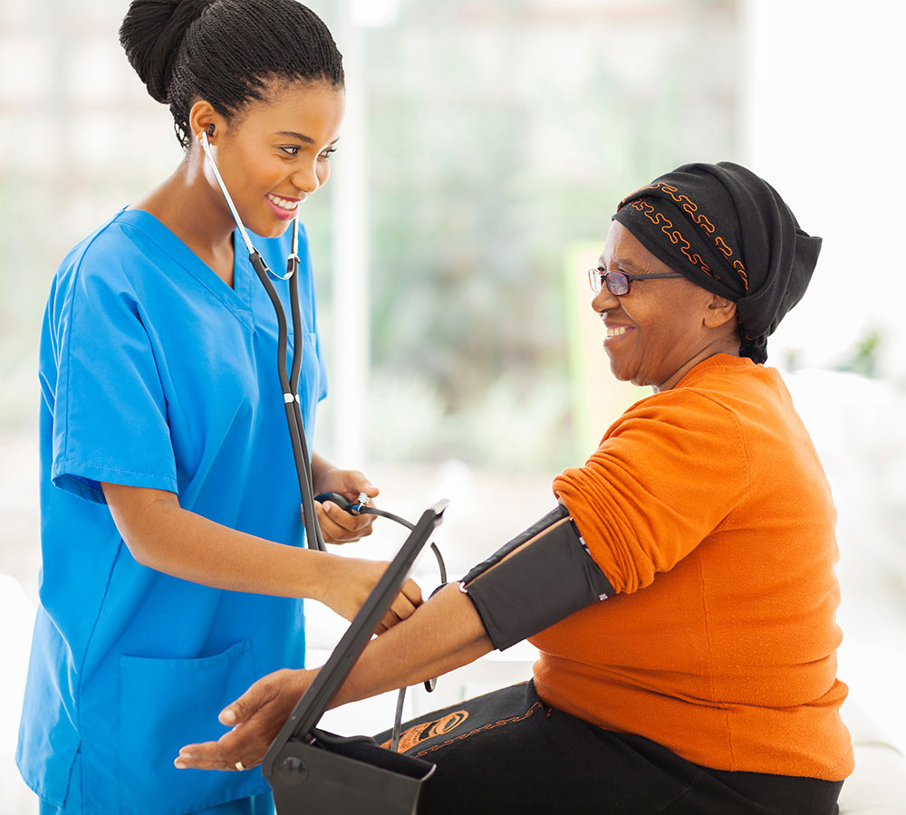 smiling african nurse checking senior patient's blood pressure